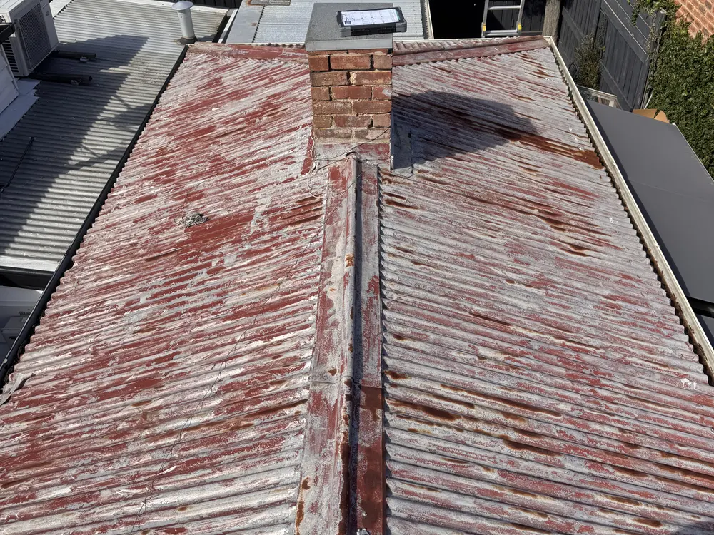 Badly rusted corrugated iron roof around a brick chimney
